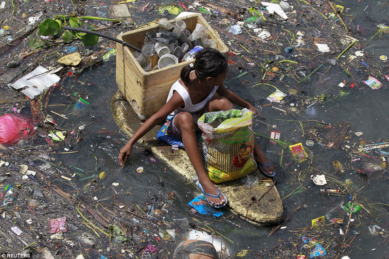 Le Gange en inde à nouveau, une fillette ramasse des contenant vides sur cette barque imrovisée.© Photo sous Copyright